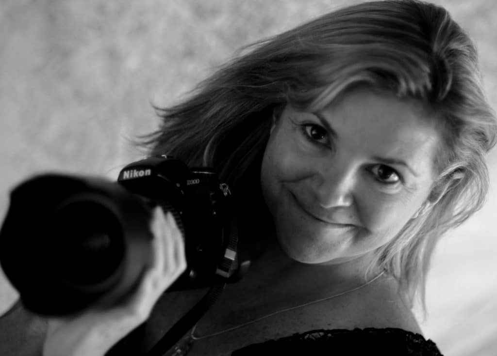 Woman holding a Nikon camera, smiling, black and white photo.