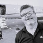 Man with glasses smiling in front of private jet aircraft.