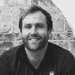 Portrait of David H., a reality capture specialist, smiling against a brick wall background.