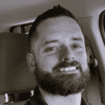 Man with a beard smiling inside a vehicle.