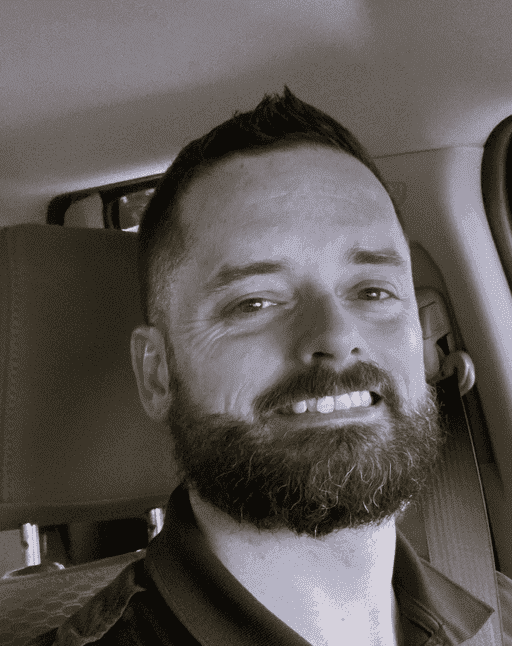 Man with a beard smiling inside a vehicle.