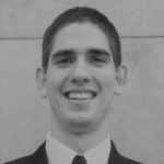 Young man in suit smiling, professional headshot, black and white photo.