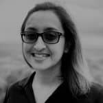 Portrait of a woman with glasses smiling outdoors in black and white.