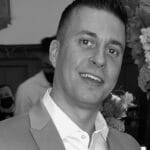 Man in a suit smiling at a formal event with floral decorations.