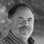 Portrait of Greg W. from NH, smiling, outdoors, black and white photo.