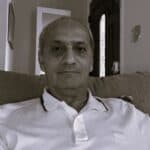 Man with short hair and white polo shirt sitting on a sofa.