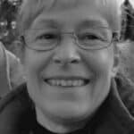 Smiling woman with glasses outdoors in black and white.
