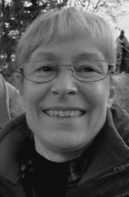 Smiling woman with glasses outdoors in black and white.