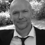 Black and white portrait of JP M. outdoors, smiling, wearing a suit and tie.