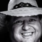 Smiling man with a hat, close-up portrait in black and white.
