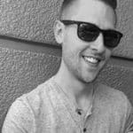 Smiling man wearing sunglasses, casual shirt, outdoors.