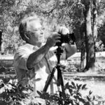 Man with camera on tripod capturing outdoor scenery in a park.