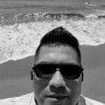 Man wearing sunglasses taking a selfie at the beach.