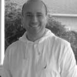 Portrait of John R. smiling outdoors in black and white.