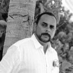 Portrait of Joseph M. standing outdoors near a tree with foliage in the background.