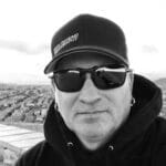 Man wearing cap and sunglasses with cityscape background.