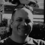 Portrait of Kevin D. smiling outdoors with sunglasses on head.