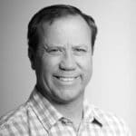 Black and white portrait of Kyle T. smiling, wearing a checkered shirt.