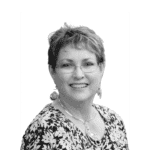 Portrait of Linda B. smiling, wearing glasses and jewelry.