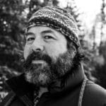 Man with a beard wearing a knit hat and outdoor jacket.