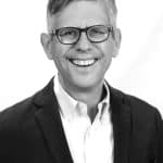 Portrait of a smiling man with glasses in a suit.