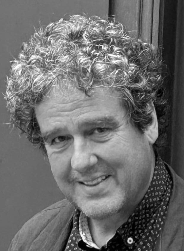 Portrait of Michael A. with curly hair, smiling, in black and white.