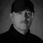 Black and white portrait of Michael L. wearing a cap and dark clothing.