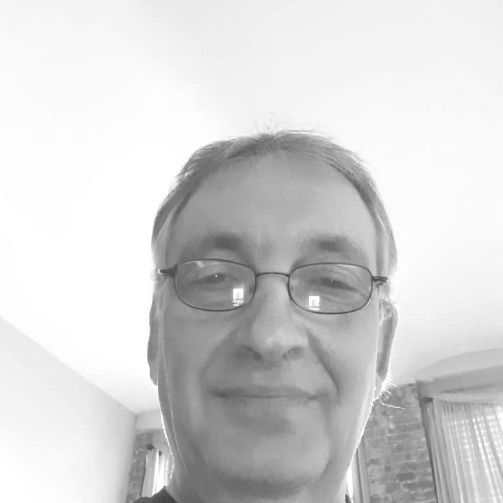 Man with glasses smiling in a well-lit room.