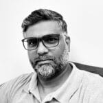 Man with glasses and beard in a polo shirt, looking at camera.