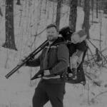 Man with camera gear hiking in snowy forest during winter.