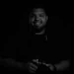 Photographer holding camera, smiling, in a dark setting.