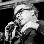 Man with glasses speaking into microphone at event.