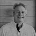 Portrait of Paul J. smiling in front of wooden wall.