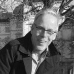 Portrait of Peter R. outdoors with trees and buildings in background.
