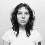 Black and white portrait of a young woman with curly hair and a serious expression.