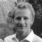 Young man smiling outdoors with trees in the background.