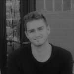 Young man with short hair smiling outdoors in black and white.