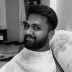 Young man with beard smiling, sitting on a sofa in black and white.