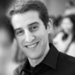 Smiling man in black shirt at a professional event, blurred background.