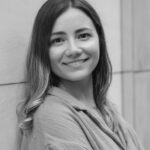 Portrait of Yulia G. smiling, standing against a wall.