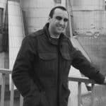 Man smiling at a construction site with modern buildings in background.