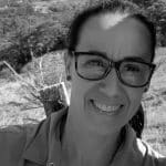Black and white portrait of Marylene H. smiling outdoors with glasses.