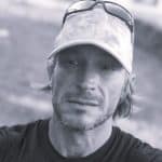 Man with sunglasses and cap outdoors, looking thoughtful.