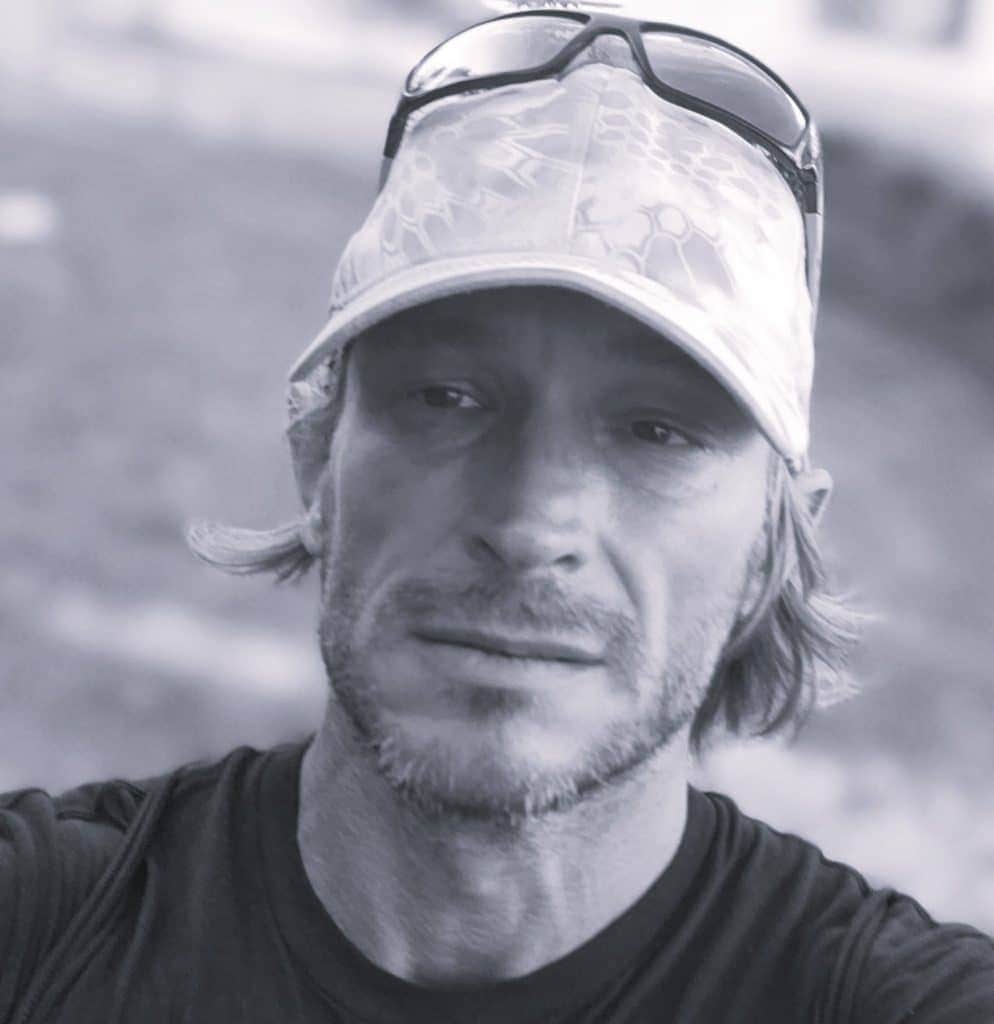 Man with sunglasses and cap outdoors, looking thoughtful.