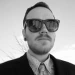 Man wearing sunglasses and suit in outdoor setting.