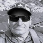 Man wearing sunglasses and cap fishing on a river.