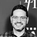 Portrait of Tony V. smiling, wearing glasses and a plaid shirt.