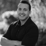 Portrait of Robert K. smiling outdoors in black and white.