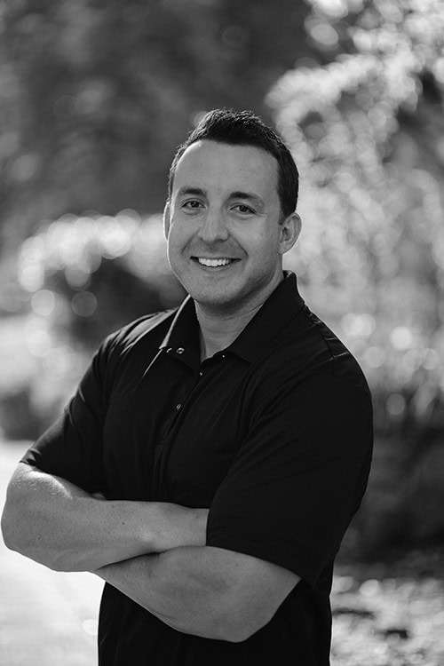 Portrait of Robert K. smiling outdoors in black and white.