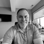 Portrait of Greg S. smiling in a modern office with natural light.